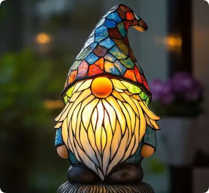 Verlicht tuinkabouterlampje met blauwe mozaïekmuts, lange witte baard en oranje neus, voor een wazige achtergrond met bloemen. 13