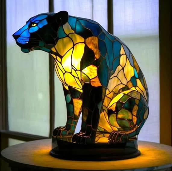 Zittende zwarte panter als lamp in blauw, groen en geel glasmozaïek, op een ronde voet voor een raam. 16