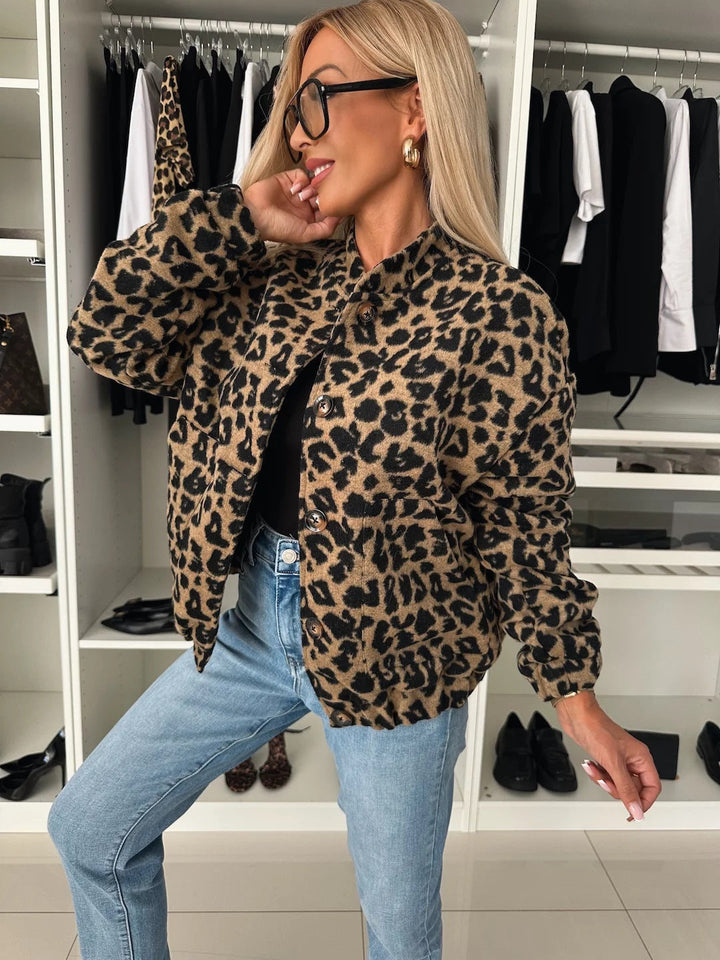 Model in een walk-in closet draagt het overhemd met luipaardprint open over een zwarte top en een spijkerbroek, in zijaanzicht. 1