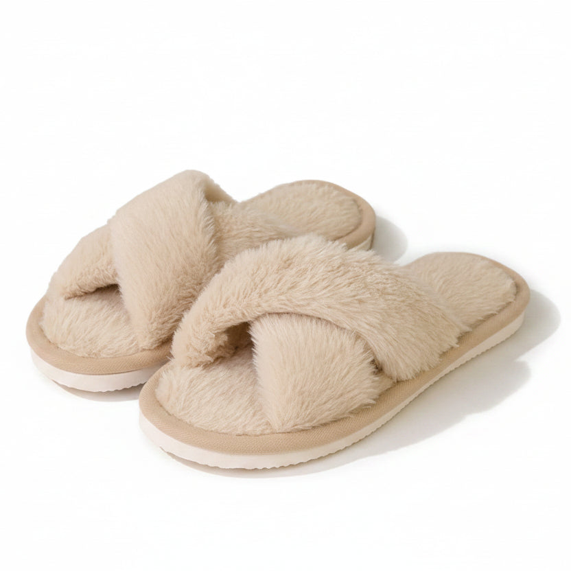 Paar beige pluche slippers met gekruiste banden, schuin van voren gefotografeerd op een witte achtergrond, zonder model. 1