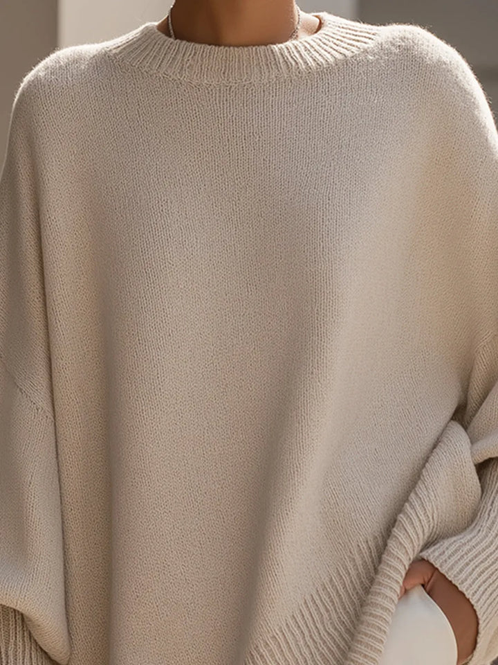 Close-up van de beige gebreide stof, het geribde ronde kraagje en de ruime schouder van de trui. 2