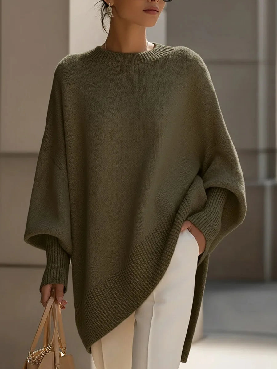Model draagt de oversized trui in olijfgroen met witte broek en een beige tas in de hand. 7