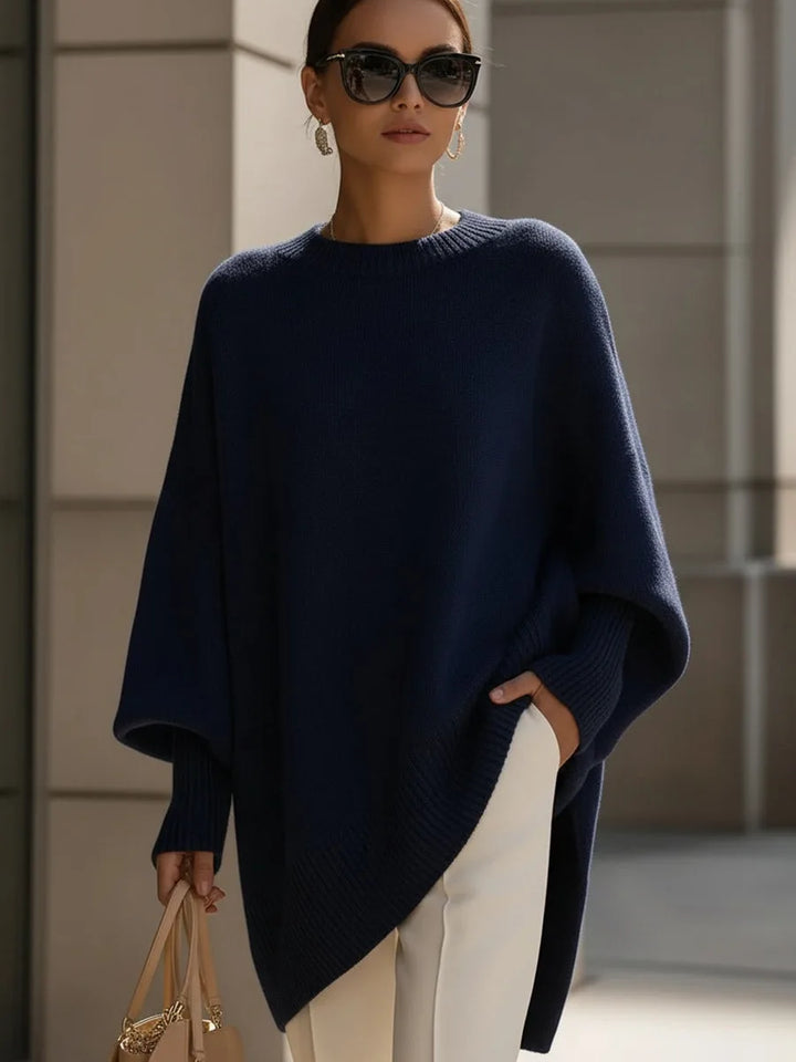 Model draagt de oversized trui in donkerblauw met witte broek, zonnebril en beige tas. 8