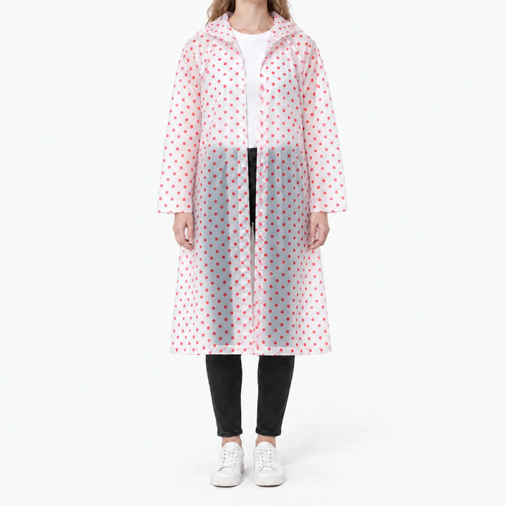 Vrouw in een doorzichtige regenjas met rode stippen en drukknopen, open gedragen over wit shirt en zwarte broek. 10