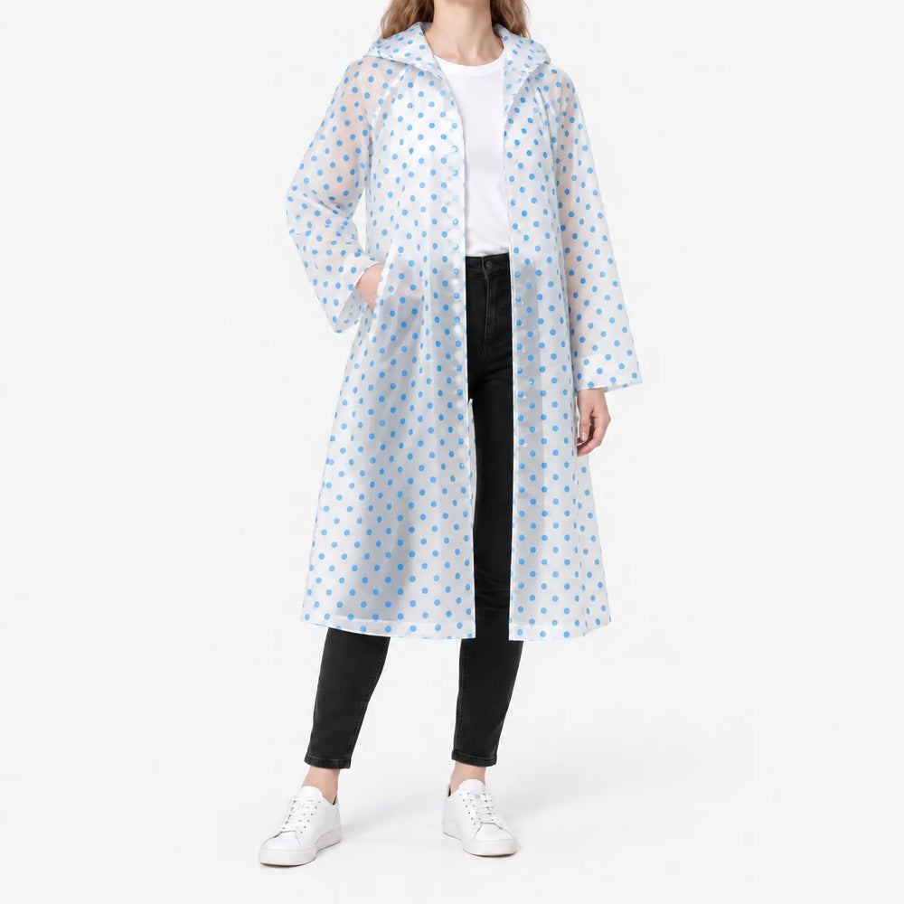Vrouw draagt een doorzichtige, openstaande regenjas met blauwe stippen over wit shirt en zwarte broek, met een hand in de zak. 2
