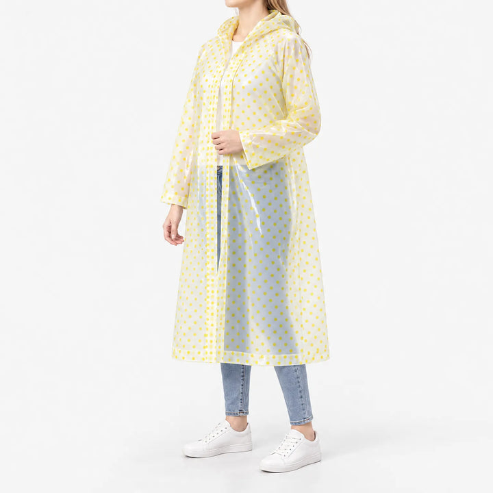 Zijaanzicht van een doorzichtige regenjas met gele stippen, gedragen met jeans en witte sneakers, met capuchon en drukknopensluiting. 5