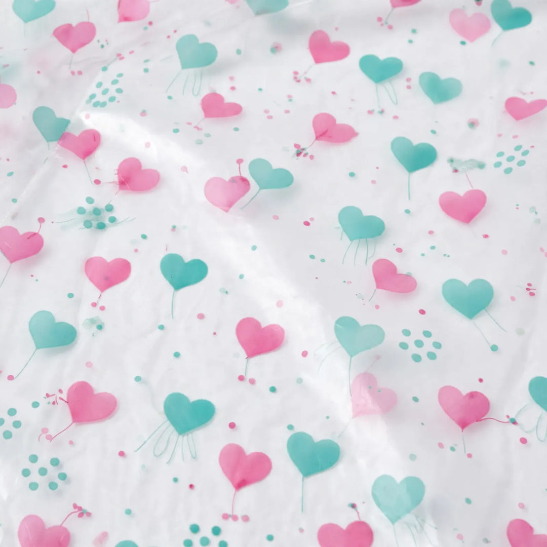 Close-up van het doorzichtige regenjasmateriaal met roze en turquoise hartjes en kleine stippen als print. 6