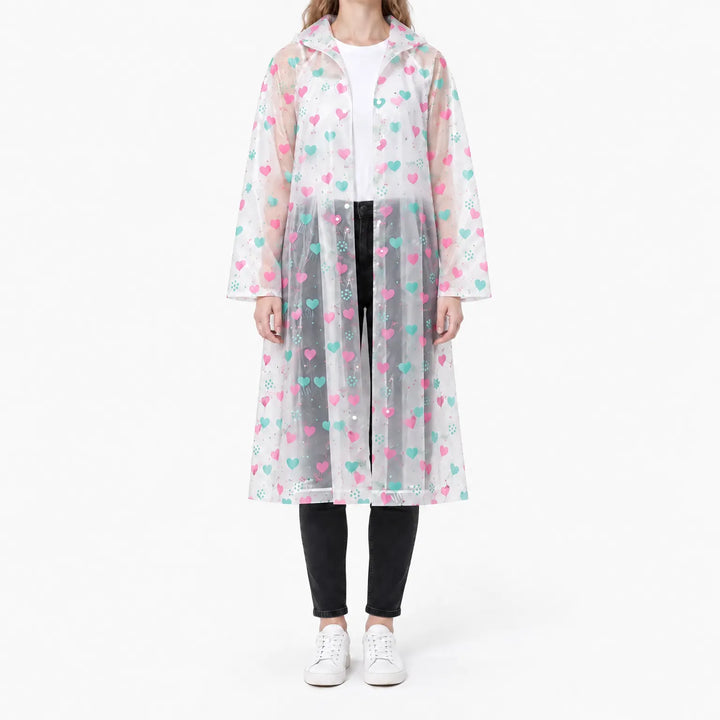 Vrouw draagt de doorzichtige regenjas met roze en turquoise hartjesprint, open over wit shirt en zwarte broek. 7