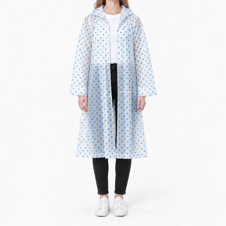 Vrouw in een doorzichtige regenjas met blauwe stippen en capuchon, open gedragen over wit shirt, zwarte broek en witte sneakers. 9