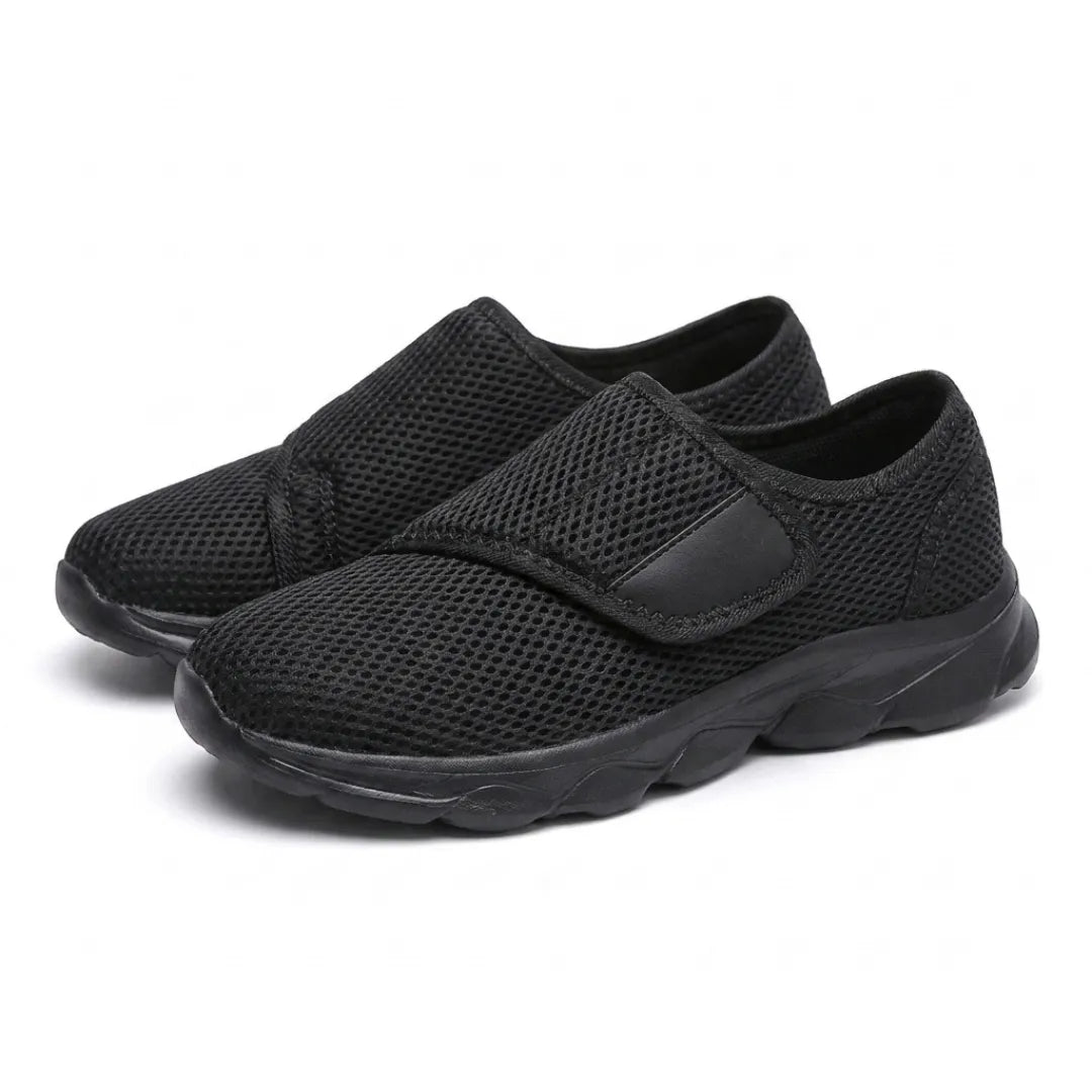 Schuin aanzicht van een paar geheel zwarte mesh schoenen met klittenbandsluiting en zwarte zool. 16
