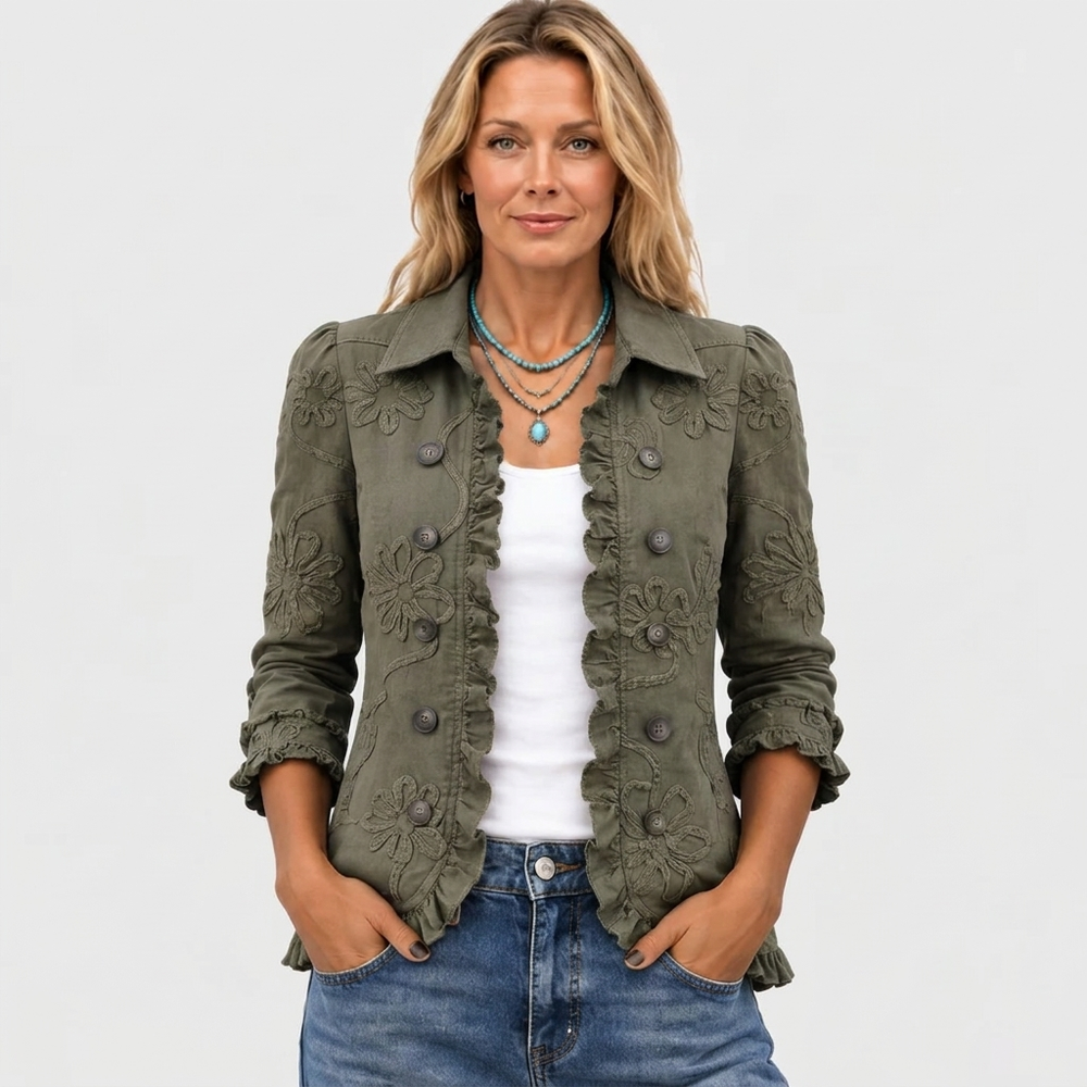 Model draagt het olijfgroene jasje open van voren met witte top, spijkerbroek en turquoise kettingen, handen in de zakken. 2