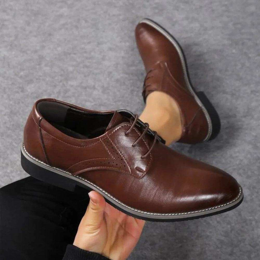 Donkerbruine nette schoen in de hand gehouden boven een grijs tapijt, met de tweede schoen op de achtergrond. 2