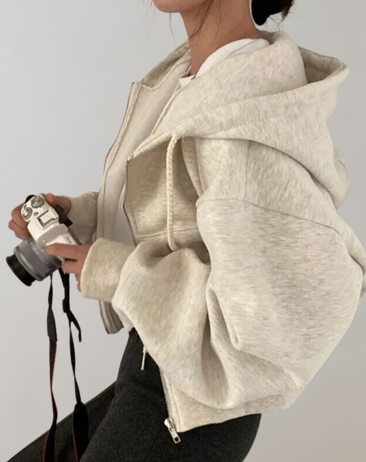 Zijaanzicht van de lichtgrijze gemêleerde hoodie met ritssluiting, wijde capuchon en ruime mouwen, gedragen door een model met camera in de handen. 2