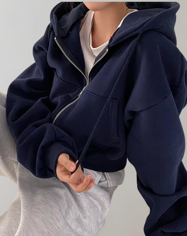 Model draagt de donkerblauwe hoodie met open rits over een wit shirt en lichtgrijze broek, een hand houdt het trekkoord vast. 3