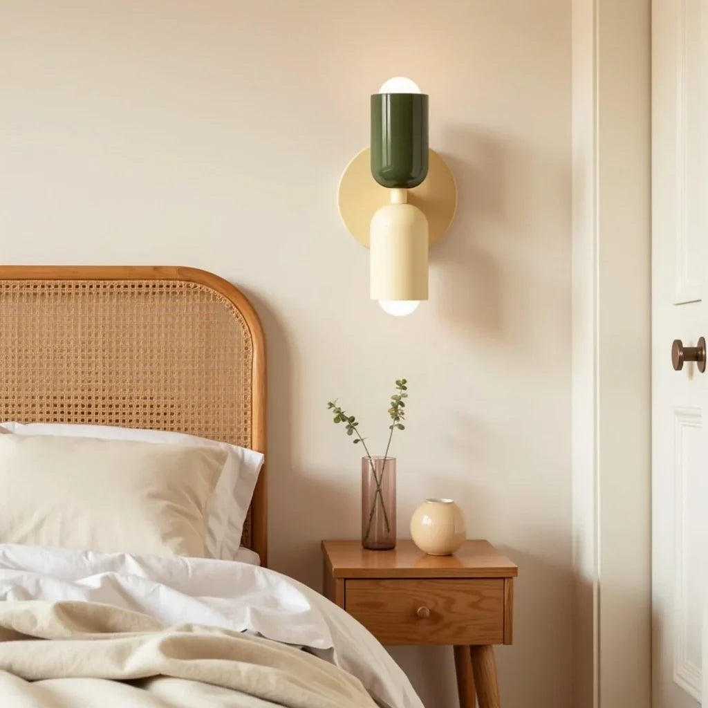 Wandlamp in donkergroen en crème naast een bed met rotan hoofdbord, boven een houten nachtkastje met glazen vaasje. 13