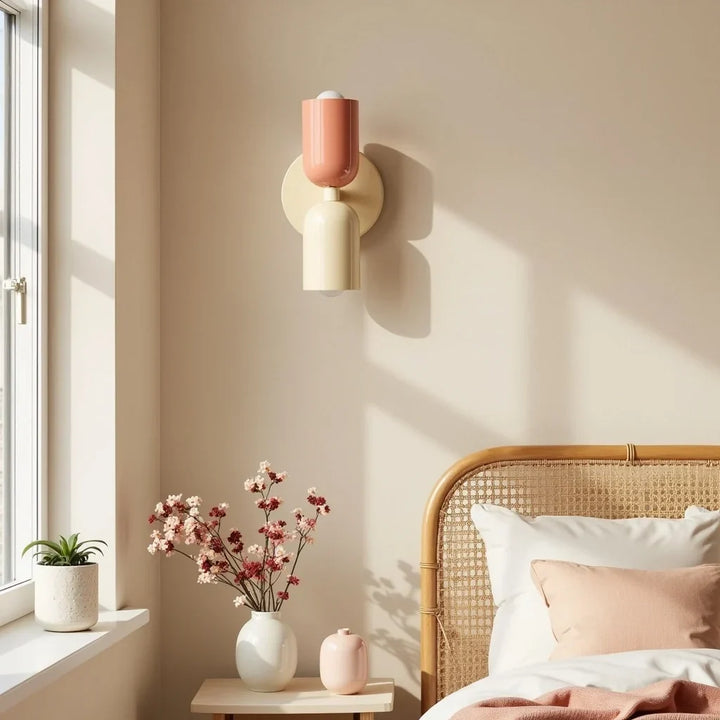 Wandlamp in zalmroze en crème naast een rotan hoofdbord, met zonlicht dat schaduwen op de beige muur werpt. 2