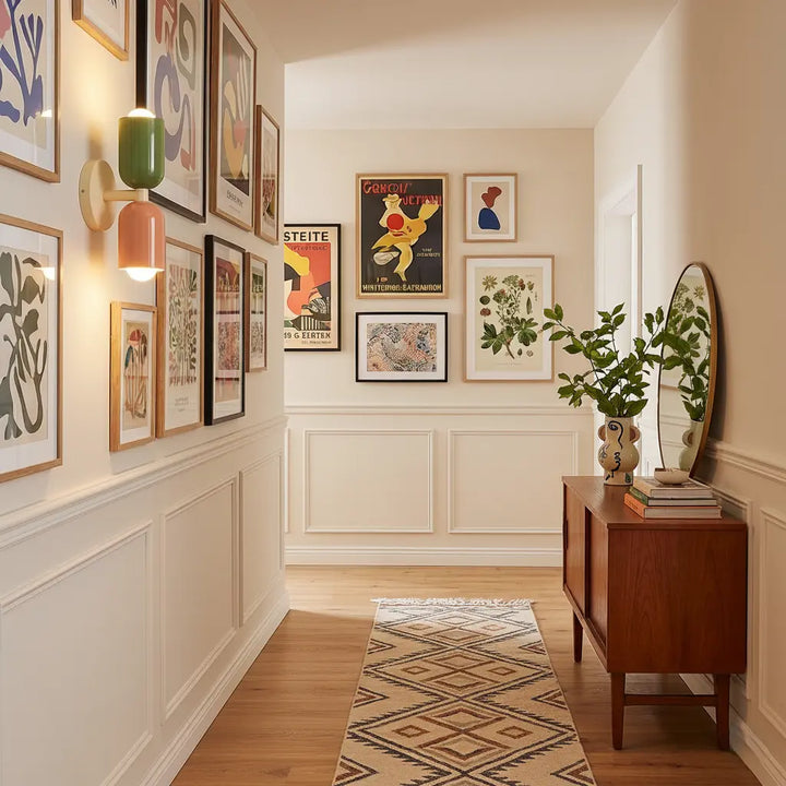 Wandlamp in groen en zalmroze in een gang vol ingelijste posters, boven een houten dressoir en een gestreepte loper. 3