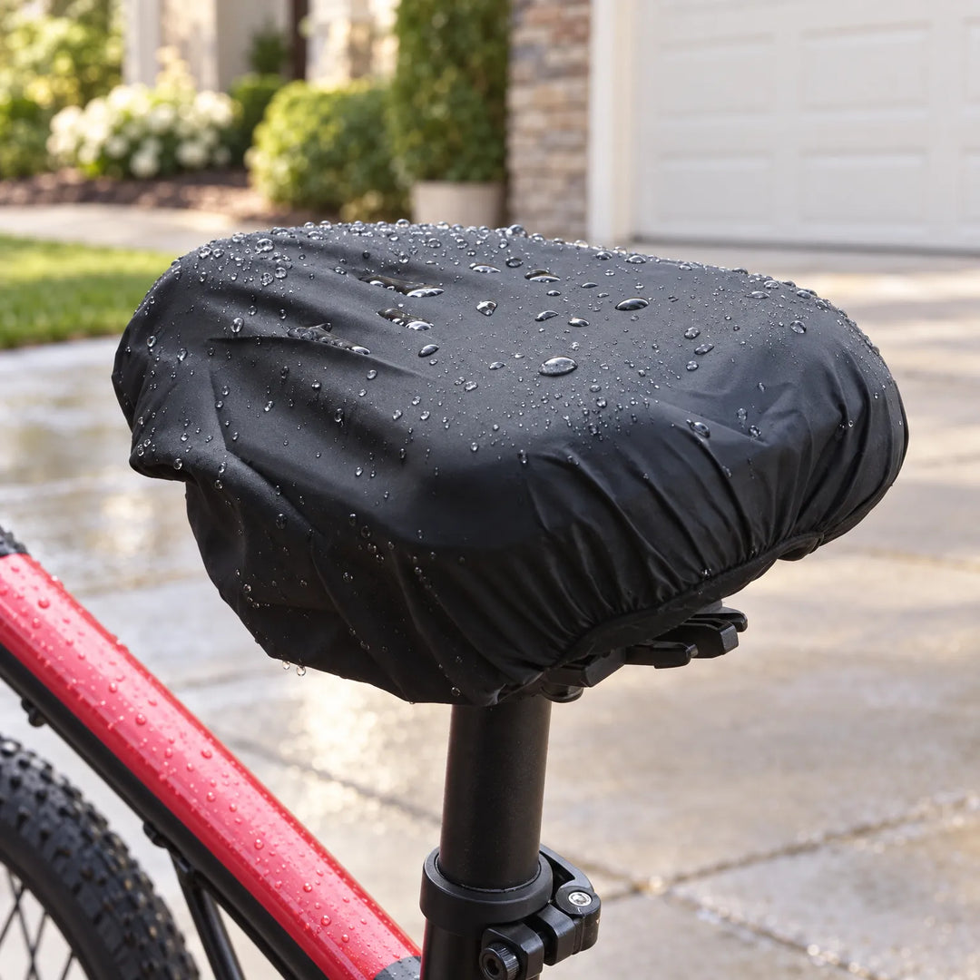 Zwarte zadelhoes met regendruppels over het zadel van een rode fiets, geparkeerd op een natte oprit voor een garage. 1