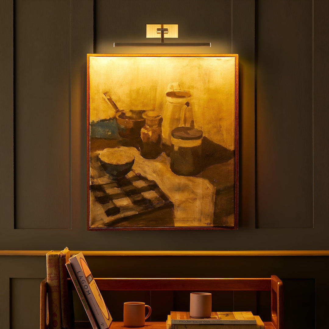 Aanstaande messing schilderijlamp die het ingelijste stilleven in warm goudkleurig licht zet, in een donkere kamer 5