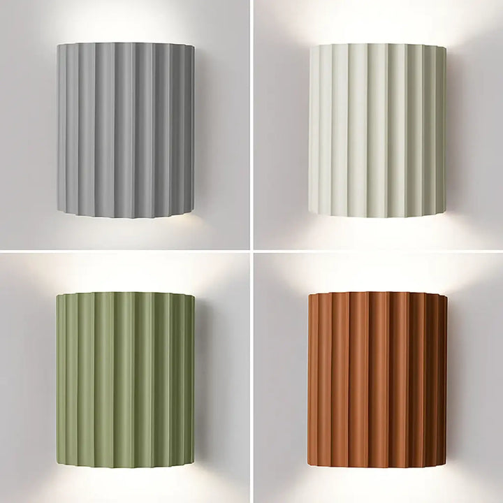Vier geribbelde wandlampen naast elkaar in grijs, wit, groen en terracotta, alle aan met omhoog en omlaag schijnend licht 1