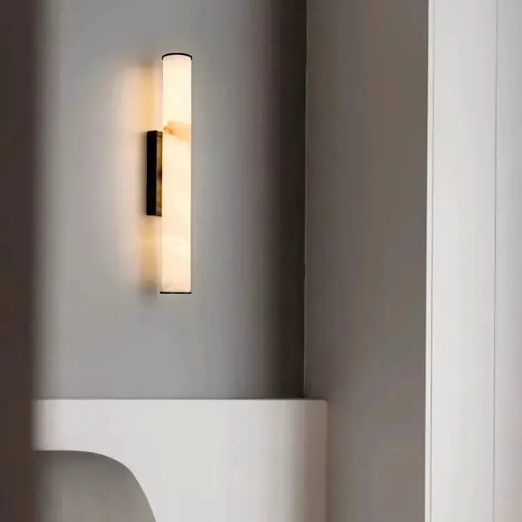 Wandlamp met zwarte afwerking en gemarmerde lichtbuis in een grijs interieur met een witte nis en een wit meubelstuk. 20
