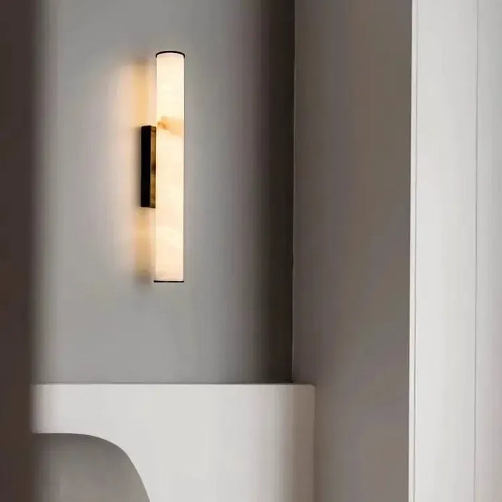 Wandlamp met zwarte afwerking en gemarmerde lichtbuis in een grijs interieur met een witte nis en een wit meubelstuk. 20