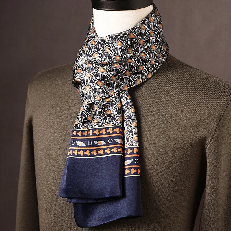 Zijden sjaal met donker golvend motief met oranje accenten en marineblauwe rand met sierstrook, op een paspop met olijfgroene trui. 11
