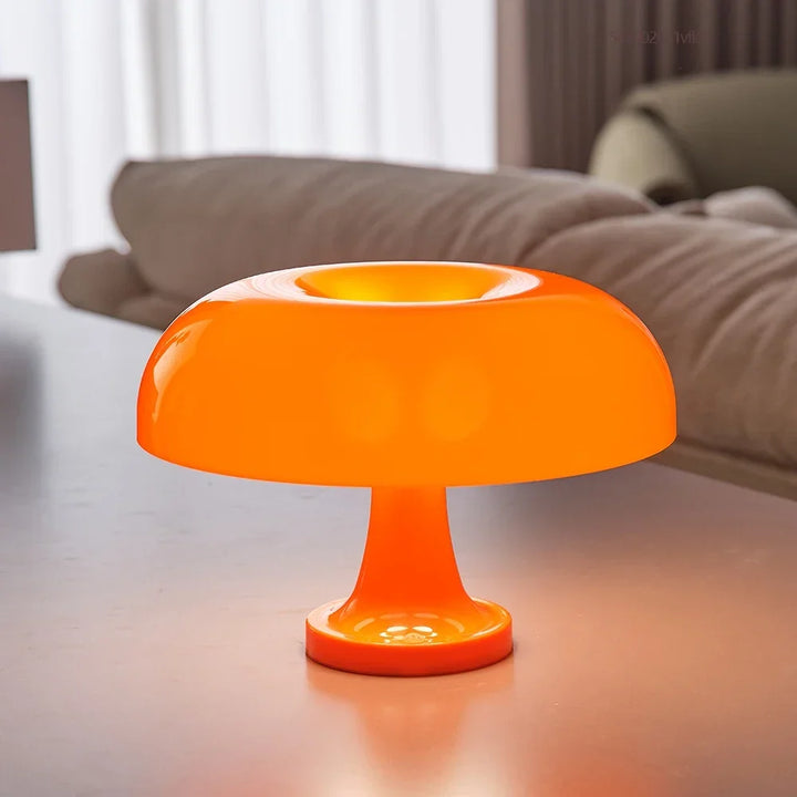 Close-up van de oranje paddenstoellamp op een tafel met de ronde kap en bolle voet, met een bank op de achtergrond. 3