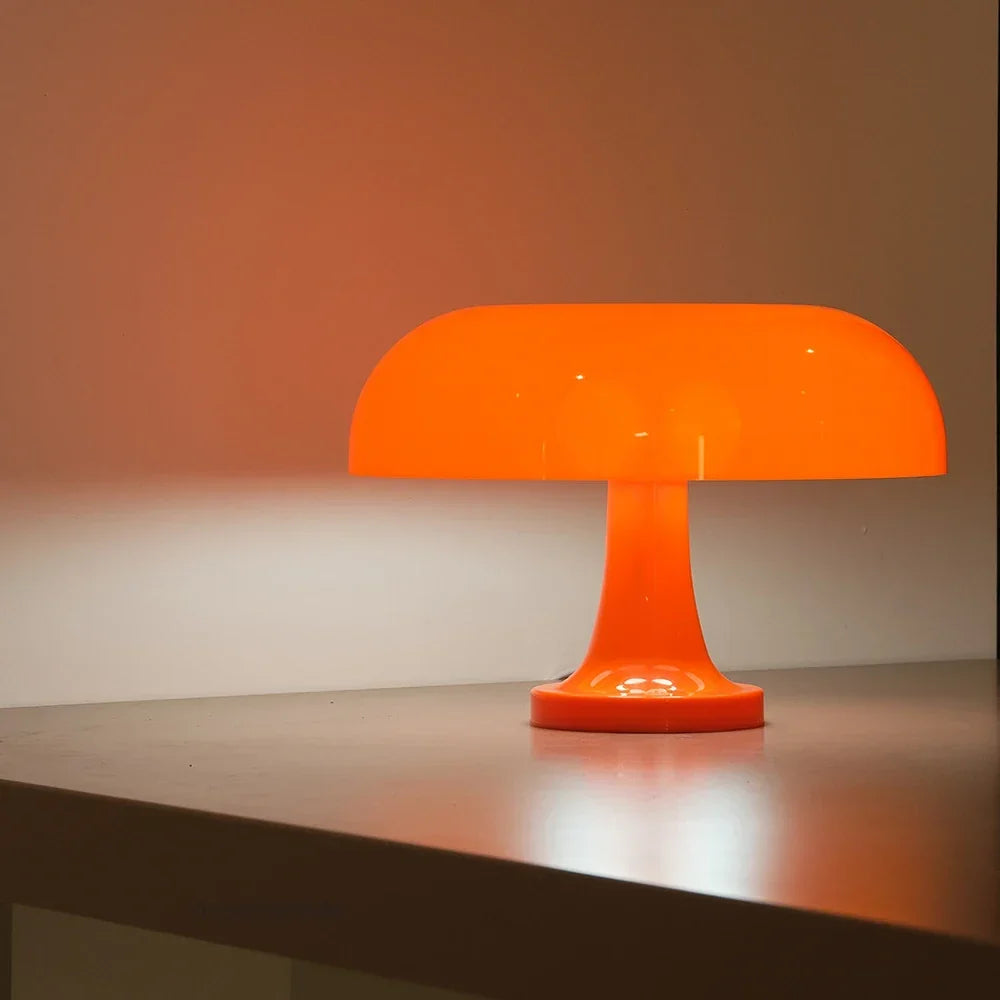 Oranje paddenstoellamp van opzij op een plank, met een warme oranje gloed op de muur erachter. 6