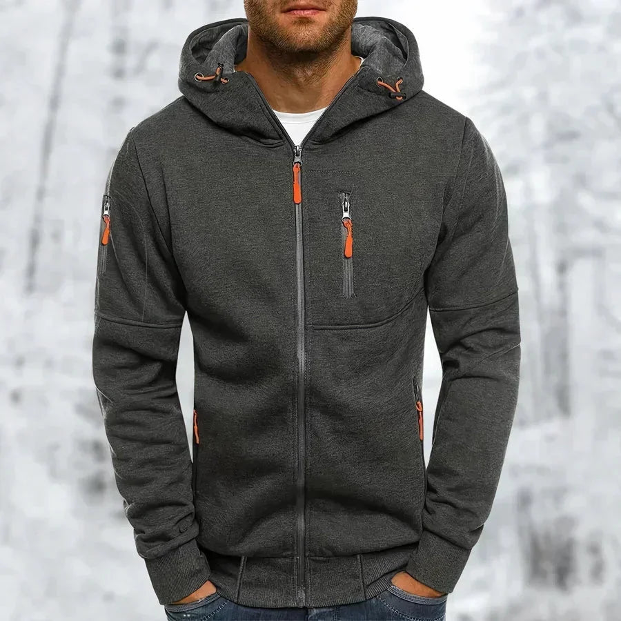 Donkergrijze hoodie met oranje ritstrekkers, voorkant gedragen door een model, met ritszakken en ribboorden aan mouwen en onderrand. 9