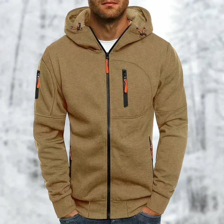 Kakibruine hoodie met zwarte rits en oranje ritstrekkers, voorkant gedragen door een model, met losse capuchon en ribboorden. 10