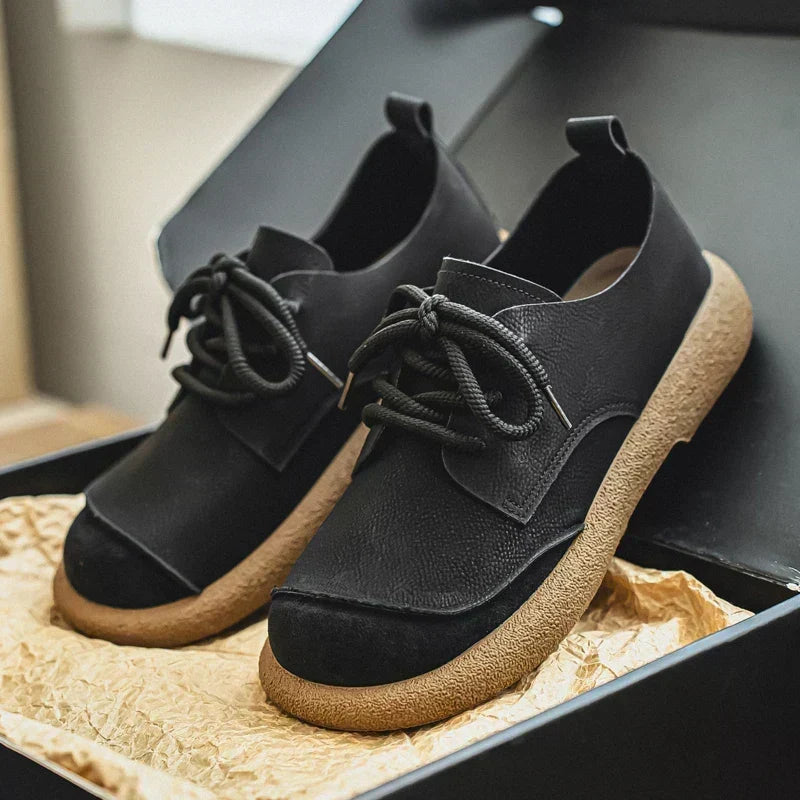 Paar zwarte veterschoenen met brede beige rubberen zool, in een open doos met verfrommeld kraftpapier. 12