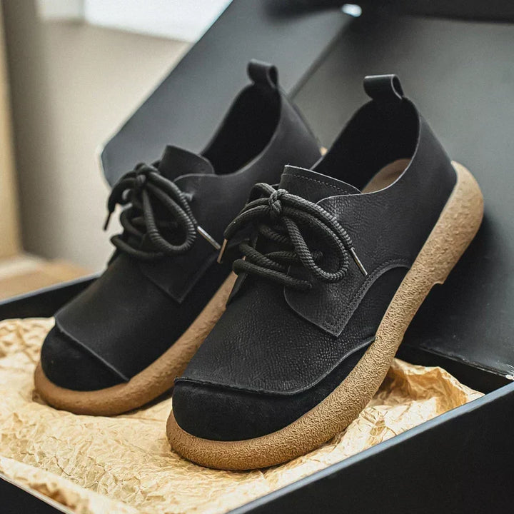 Paar zwarte veterschoenen met brede beige rubberen zool, in een open doos met verfrommeld kraftpapier. 12