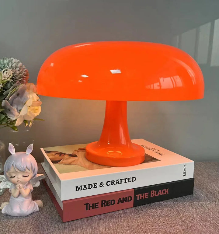 Oranje paddenstoellamp op een stapel boeken, met een bloemstuk en een klein engelenbeeldje ernaast. 7