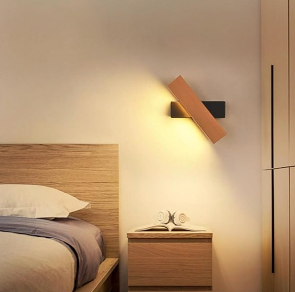 Draaibare houten wandlamp met zwarte bevestiging boven een nachtkastje naast een bed met houten hoofdbord, warm brandend. 6