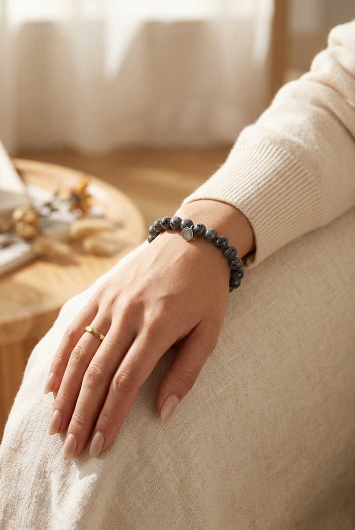 Pols van een vrouw met grijze gevlekte kralenarmband, in een lichte woonkamer met crèmekleurige trui 1