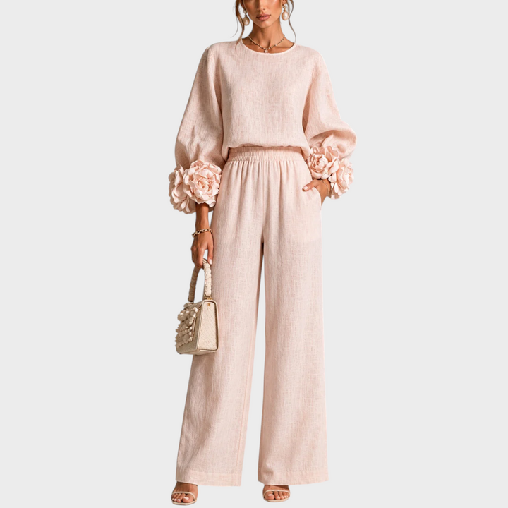 Model in roze set van top met bloemversierde mouwen en wijde broek, vooraanzicht met handtas 1