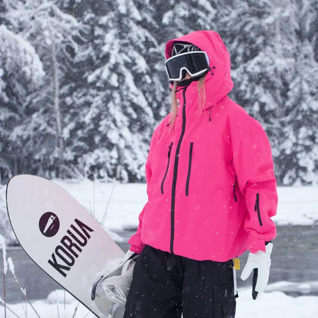 Model in felroze jas met capuchon omhoog loopt met een snowboard in de hand door een besneeuwd bos. 5