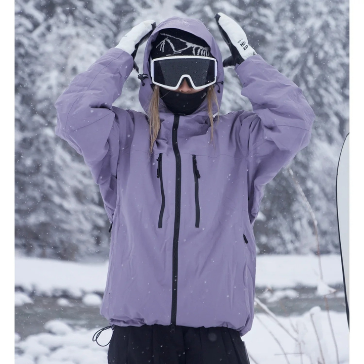 Model in lavendelpaarse jas met opgezette capuchon, handen boven het hoofd, in een besneeuwd bos met sneeuwval. 1