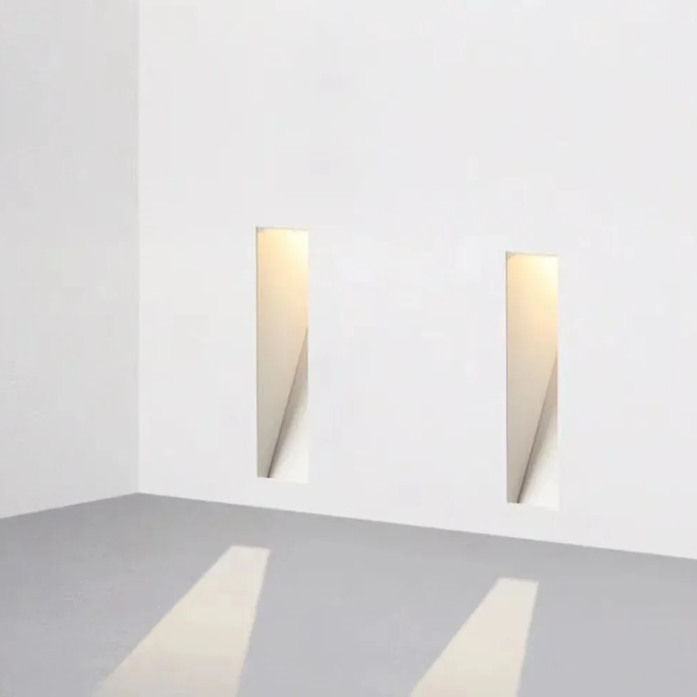 Twee smalle, verticale ingebouwde wandlampen in een witte hoek, met lichtkegels op de vloer 5