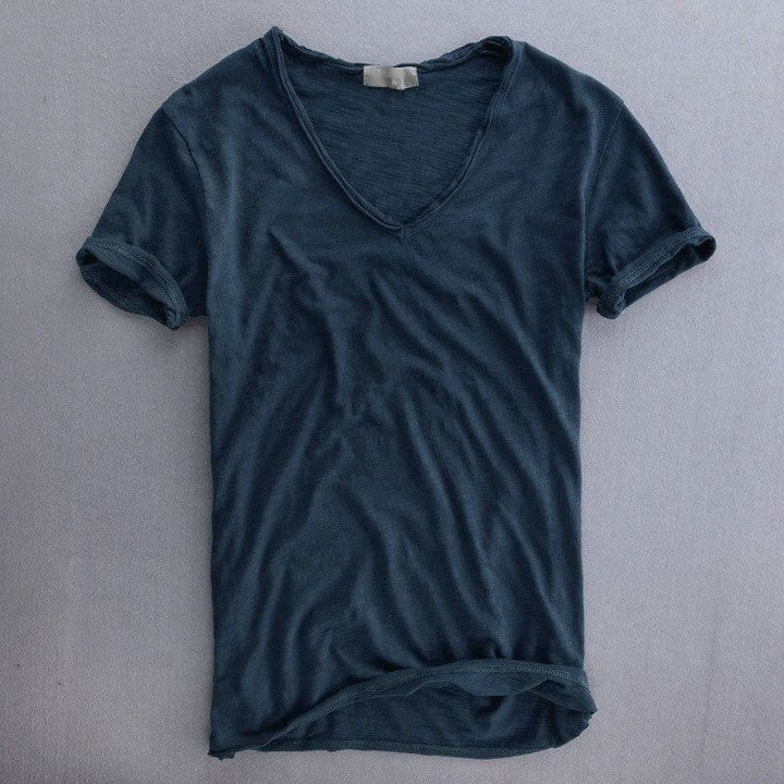 Donkerblauw T-shirt met V-hals en opgerolde mouwen, plat gefotografeerd op een grijze ondergrond, met een zichtbare vlamstructuur in de stof. 5