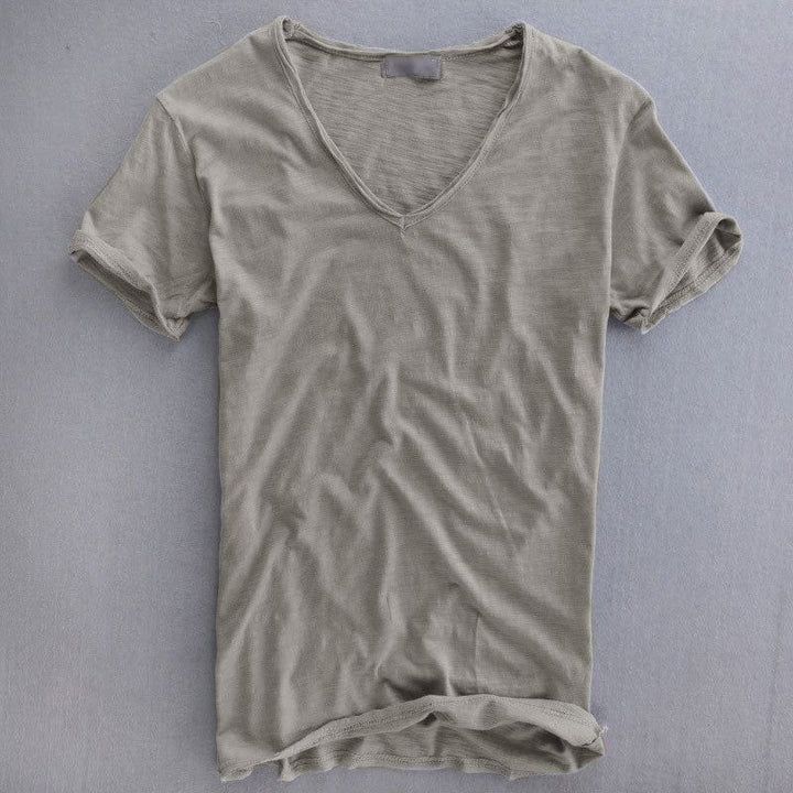Taupegrijs T-shirt met V-hals, plat neergelegd op een grijze ondergrond, met opgerolde mouwen en een lichte vlamstructuur in de stof. 1