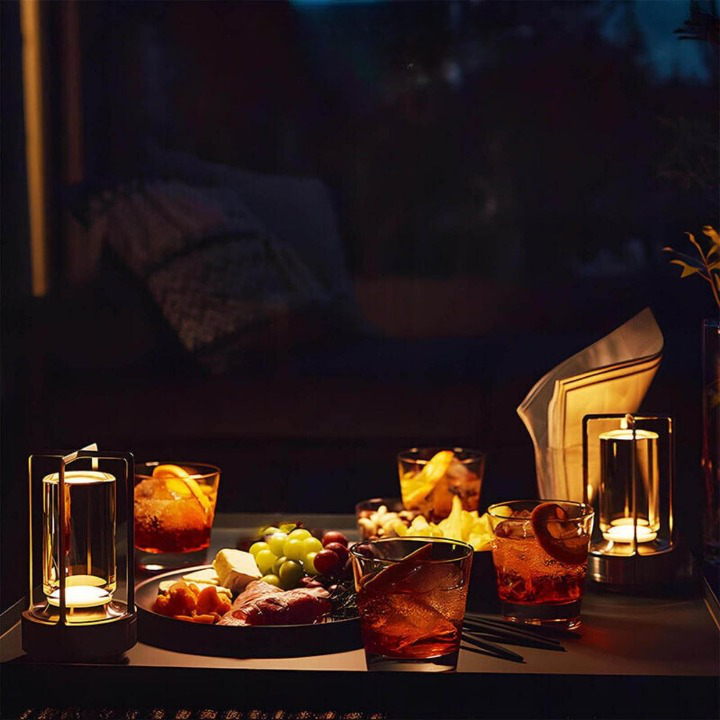 Twee brandende lampjes op een tafel met cocktails, een bord hapjes en druiven in de schemering. 6