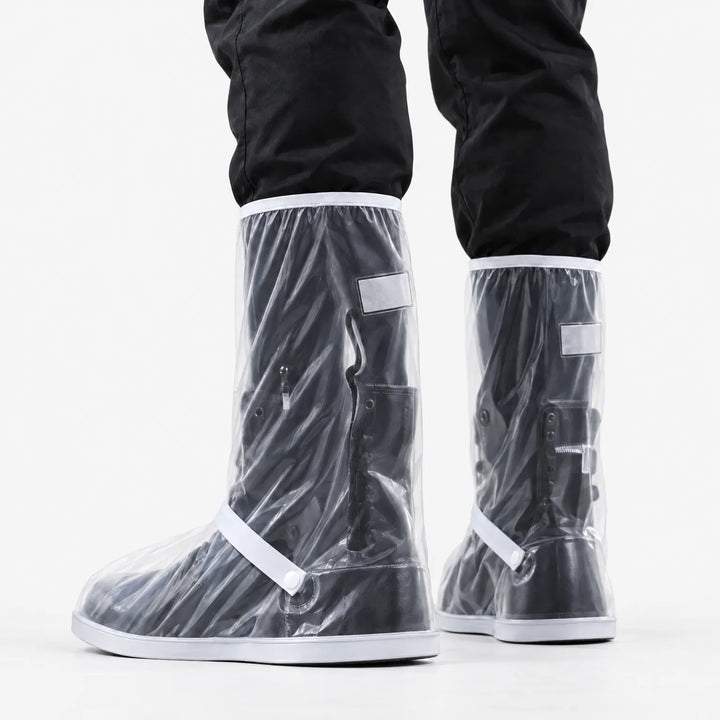 Achteraanzicht van doorzichtige regenoverschoenen met witte rand en bandje, gedragen over zwarte laarzen en onder een zwarte broek. 4