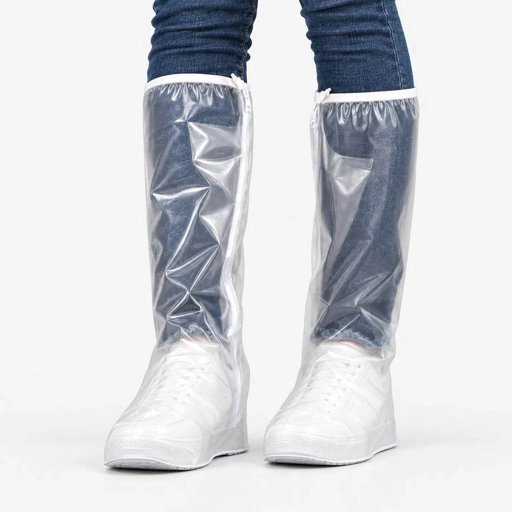 Voorkant van doorzichtige overschoenen met rits aan de zijkant en elastische bovenrand, gedragen over witte sneakers en een spijkerbroek. 2