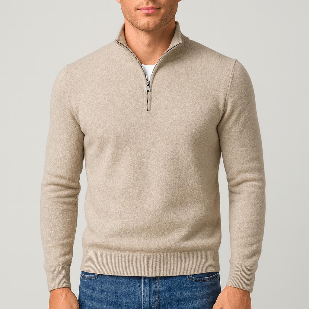 Man draagt een beige trui met opstaande kraag en halve ritssluiting, gecombineerd met een spijkerbroek en wit shirt eronder. 1