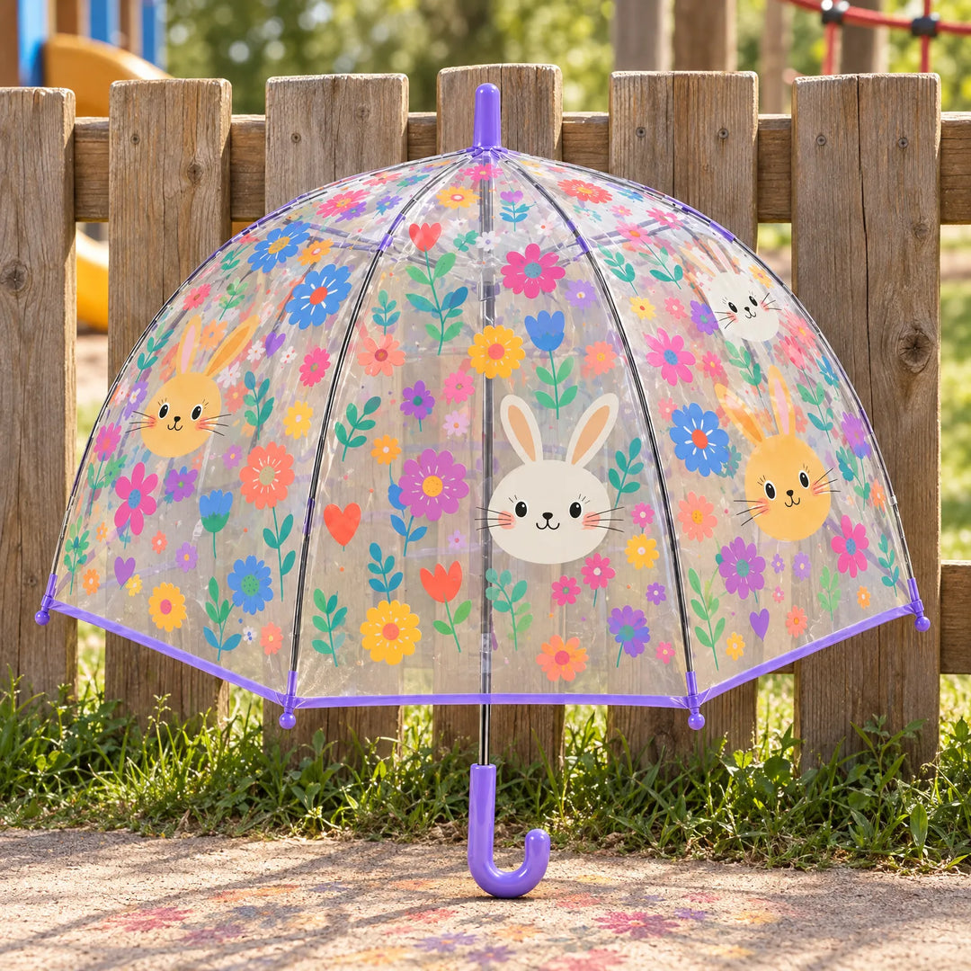 Doorzichtige koepelparaplu met konijntjes en bloemen en paarse rand en handvat, buiten tegen een houten hek neergezet. 1