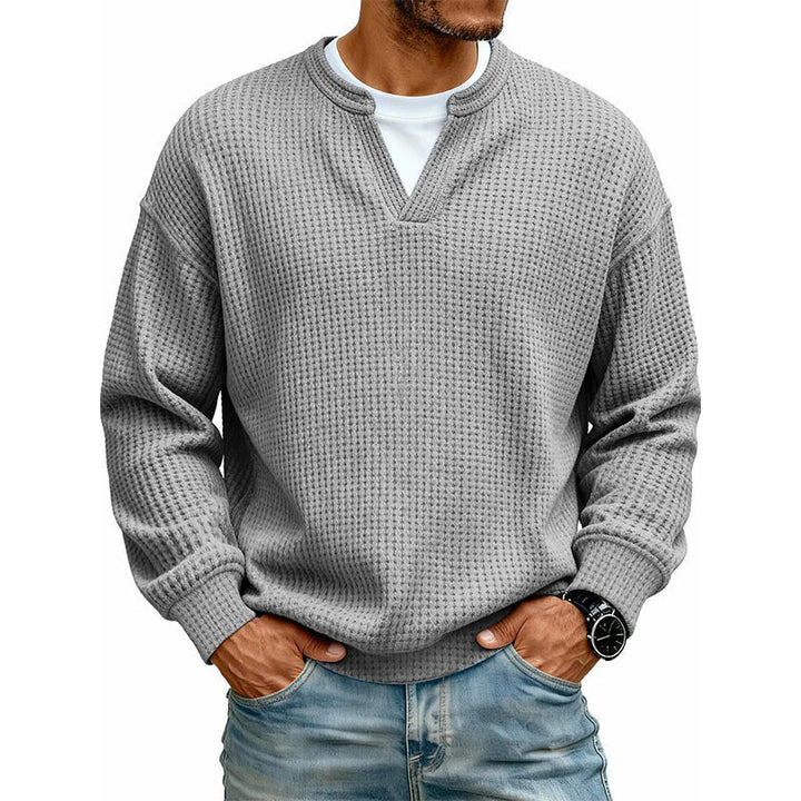 Dezelfde wafeltrui in grijs, gedragen door een model met wit shirt eronder en een spijkerbroek. 11