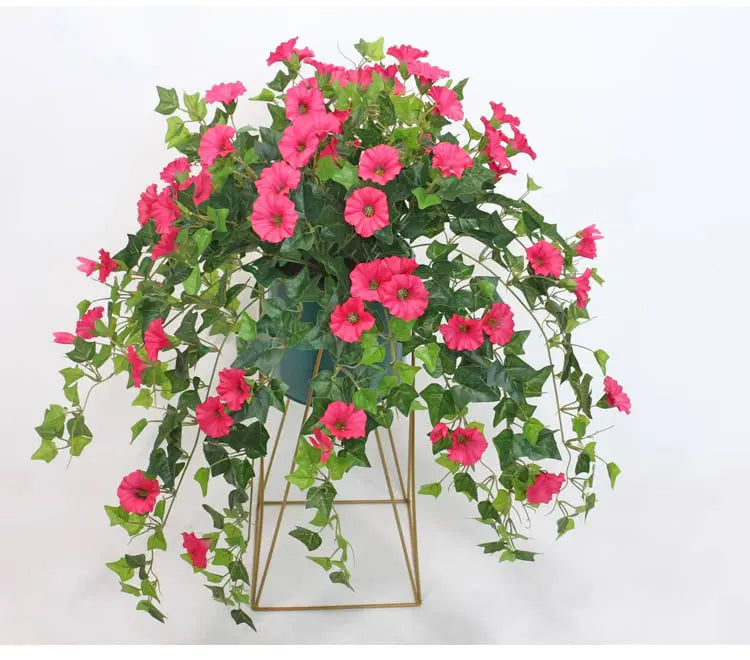 Roze kunstbloemen met overhangende groene ranken in een pot op een goudkleurig metalen standaardje. 3