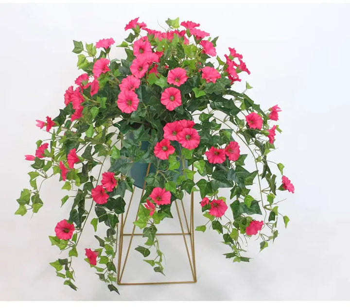Roze kunstbloemen met overhangende groene ranken in een pot op een goudkleurig metalen standaardje. 3